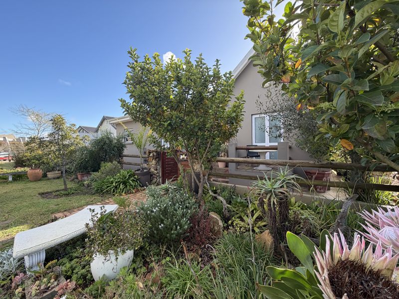 A well-maintained rear garden featuring a brick pathway, established landscaping, and a covered patio area accessible via a sliding glass door.