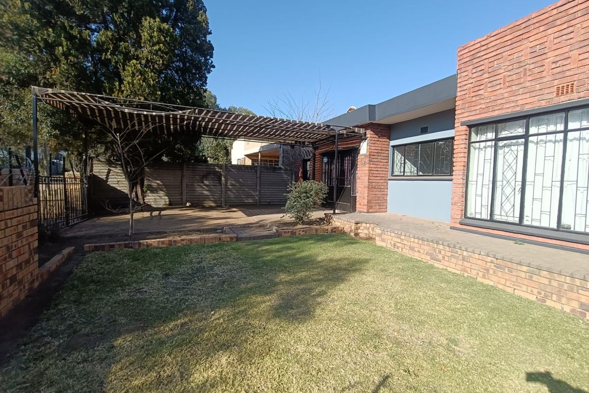 Rear exterior view featuring a brick facade, a covered patio area, and a private garden with a lawn and perimeter walling.