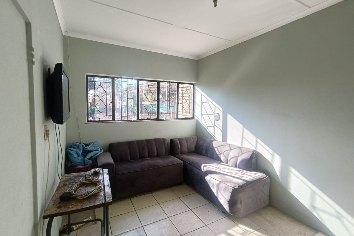 A compact living room featuring tiled flooring and security-barred windows, offering a functional space with potential for cosmetic updates.