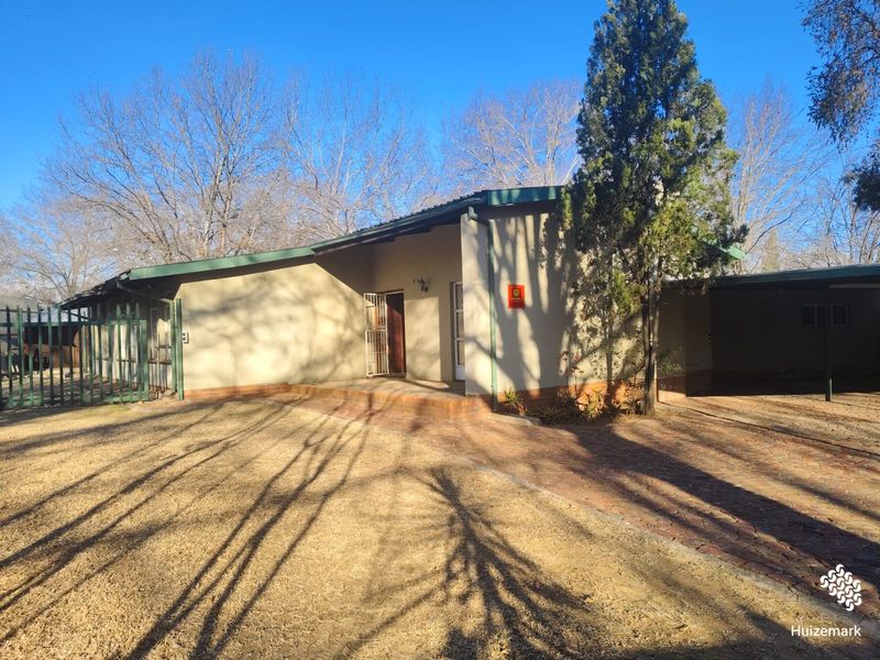Front exterior view of a single-story house featuring a brick driveway, covered entrance porch, and metal security fencing.