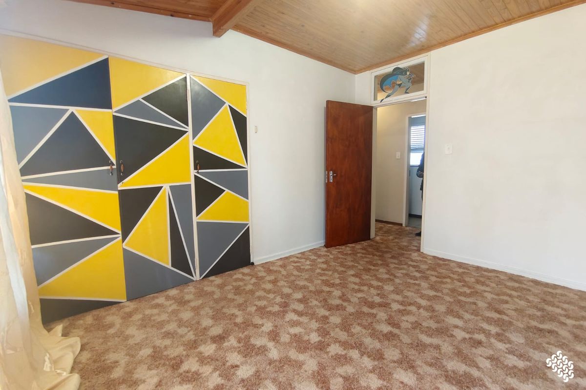 A spacious bedroom featuring a timber ceiling, built-in cupboards with a geometric design, and carpeted flooring.