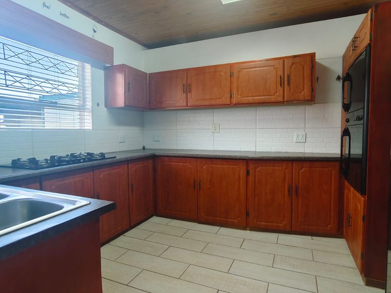 A functional kitchen featuring wooden cabinetry, built-in oven, gas hob, tiled backsplash, and tiled flooring under a wooden ceiling.