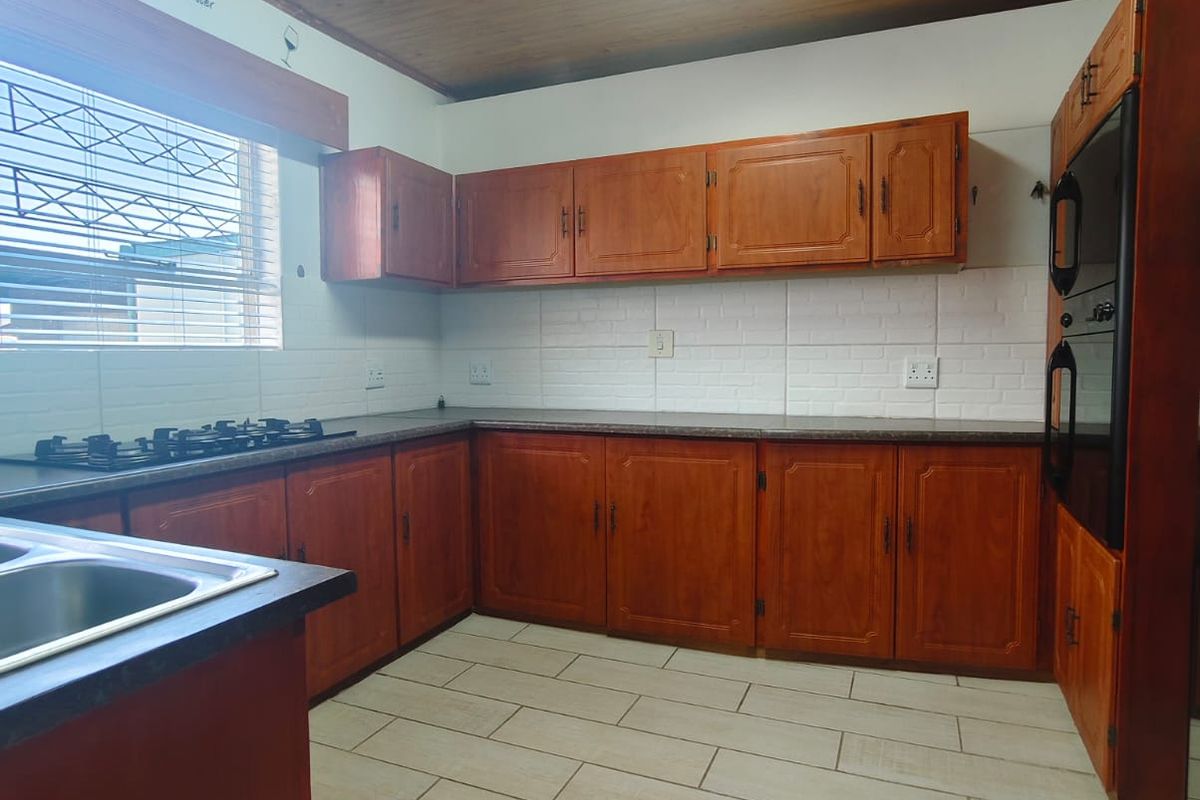 A functional kitchen featuring wooden cabinetry, built-in oven, gas hob, tiled backsplash, and tiled flooring under a wooden ceiling.