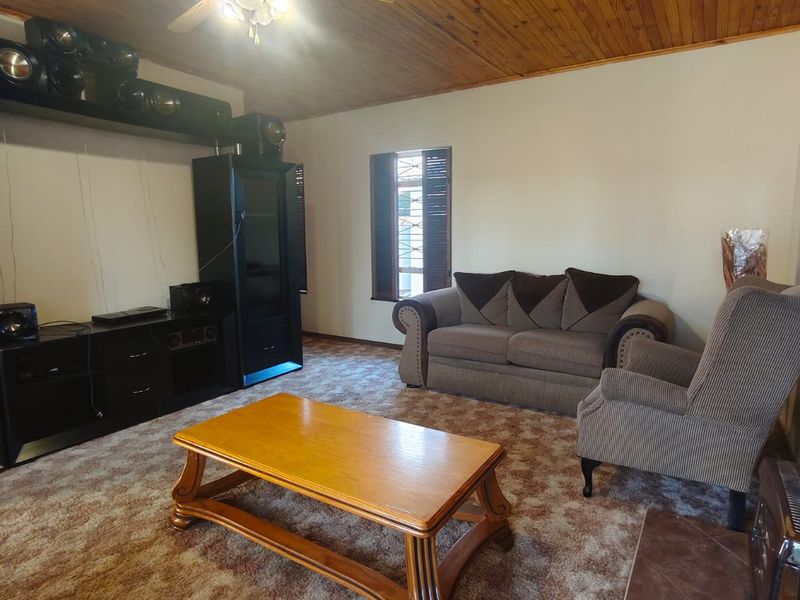 A living room featuring a timber-clad ceiling, ceiling fan, and a tiled fireplace hearth, with dated carpet flooring throughout.