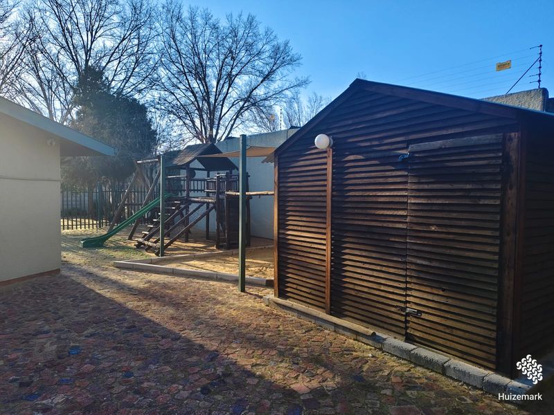 Rear garden area featuring a paved courtyard, a wooden storage shed, and a dedicated sand pit play area.