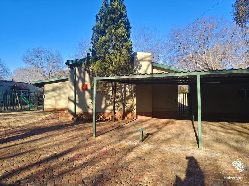 Front exterior view of the property featuring a paved brick driveway and a covered carport structure.