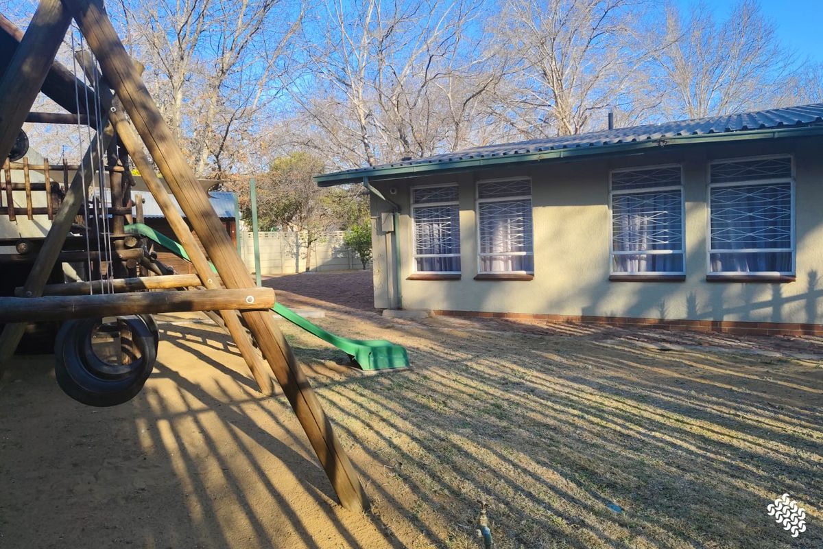 Rear view of the property featuring a garden area, security bars on windows, and a corrugated metal roof.