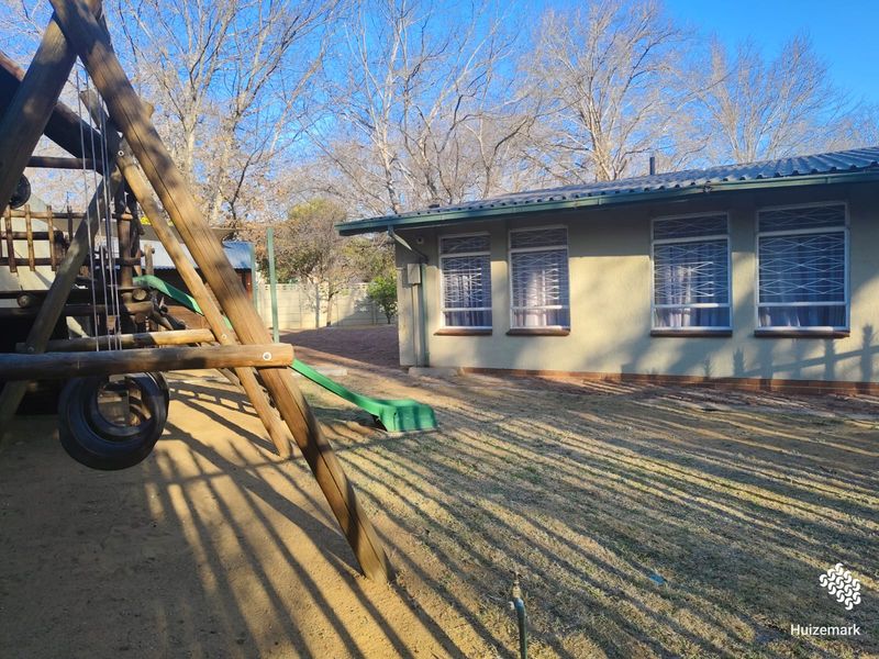 Rear view of the property featuring a garden area, security bars on windows, and a corrugated metal roof.