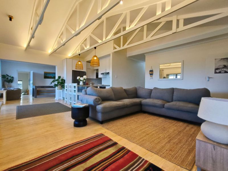Spacious open-plan living area featuring high vaulted ceilings with exposed white trusses, timber flooring, and a modern kitchen with a central island.