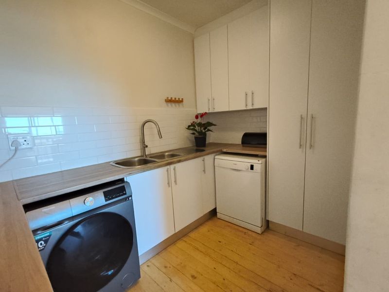 A functional scullery featuring white cabinetry, timber flooring, a stainless steel sink, and dedicated space for laundry and dishwashing appliances.