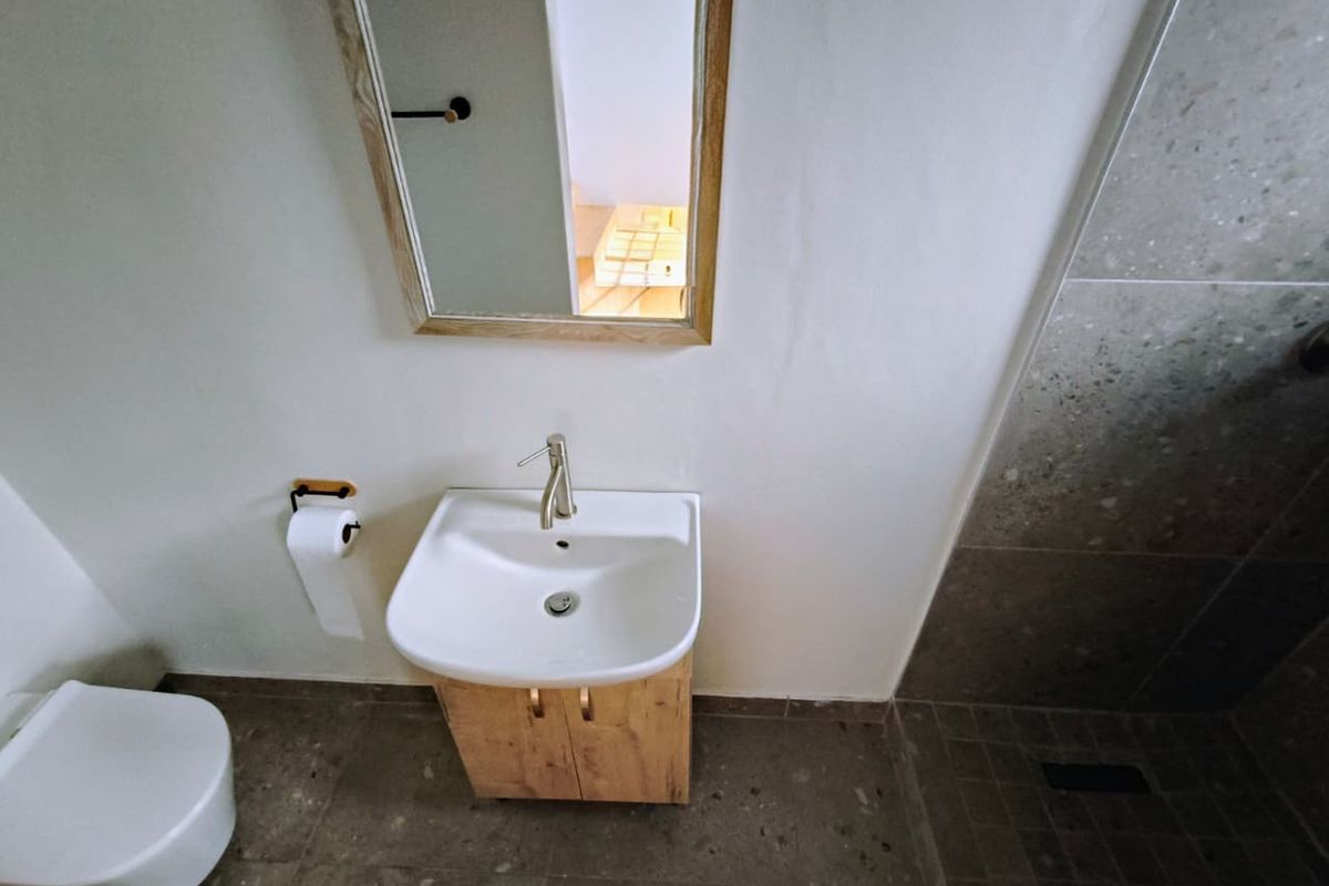 Modern bathroom featuring a vanity cabinet with a ceramic basin, wall-mounted mirror, toilet, and a walk-in shower with tiled finishes.