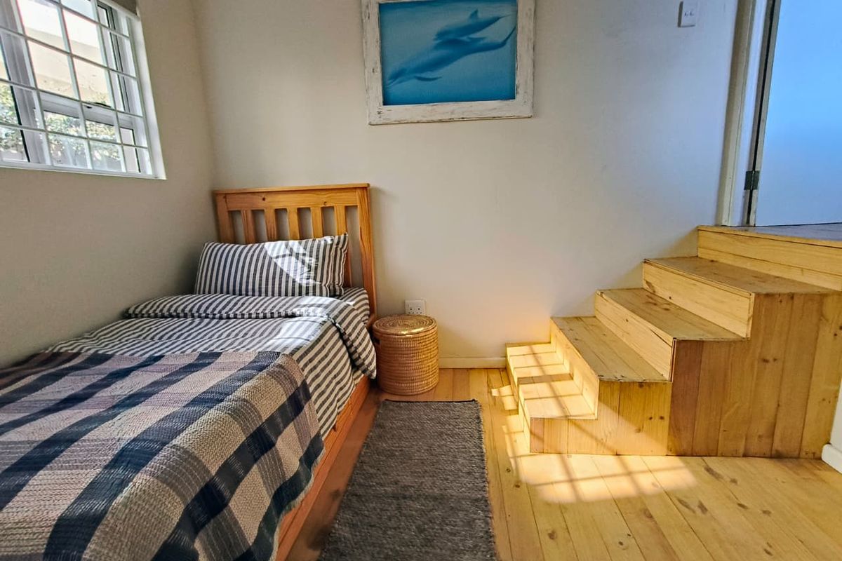 A compact bedroom featuring natural timber flooring and a built-in timber staircase leading to an elevated area.