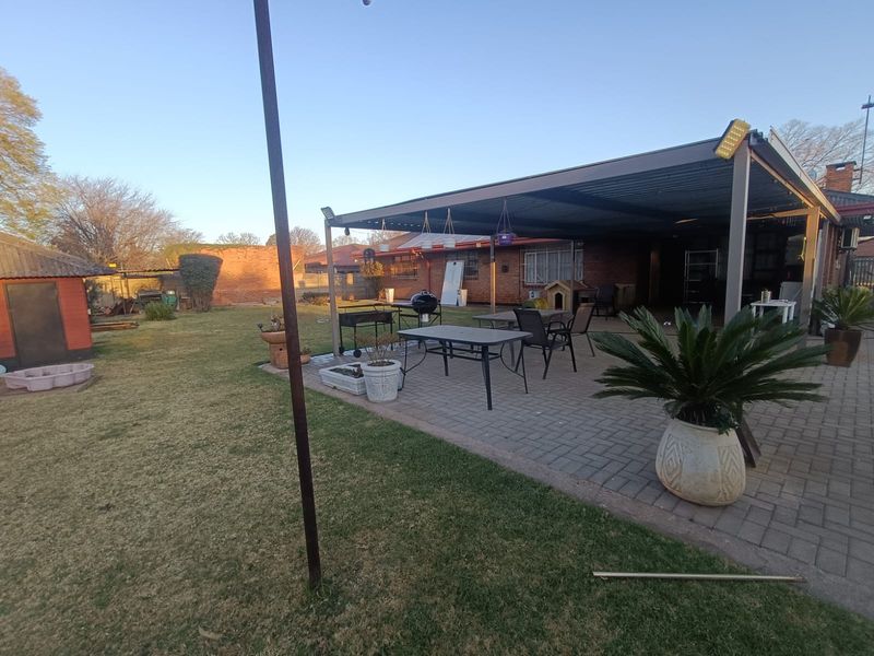 Spacious rear garden featuring a large paved patio area with a covered roof structure, ideal for outdoor entertaining.