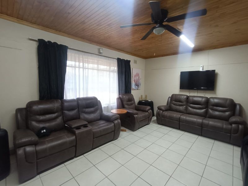 A living room featuring a timber tongue and groove ceiling, ceiling fan, and tiled flooring.