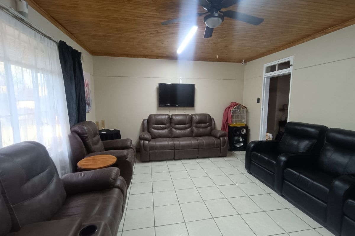 A living room featuring ceramic floor tiles and a timber tongue and groove ceiling with an integrated ceiling fan.