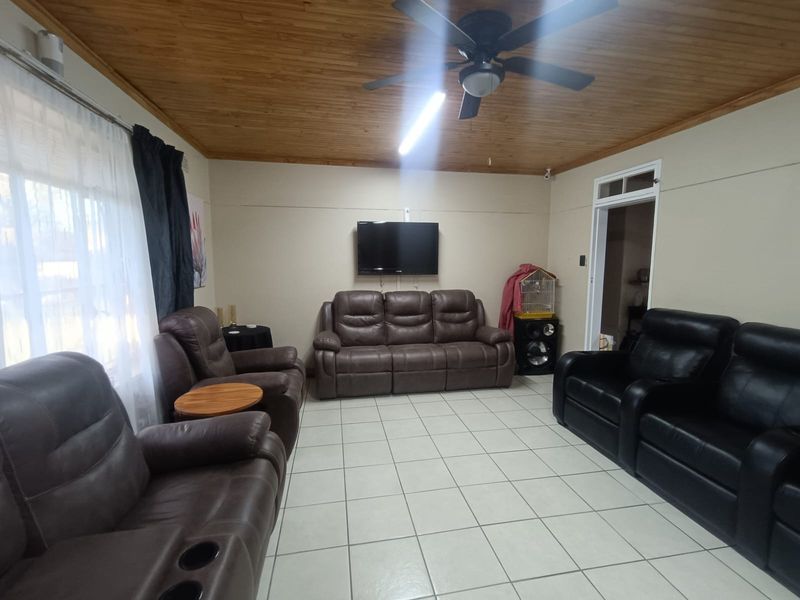 A living room featuring ceramic floor tiles and a timber tongue and groove ceiling with an integrated ceiling fan.