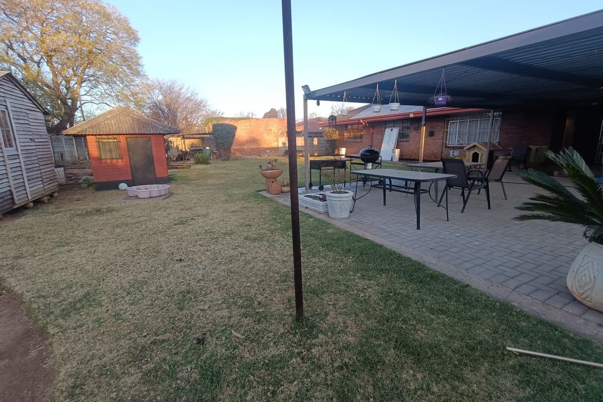 Spacious rear garden featuring a paved, covered patio area, brick exterior walls, and a detached outbuilding.