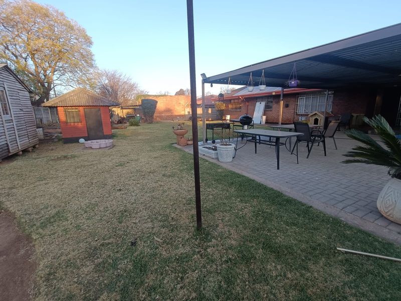Spacious rear garden featuring a paved, covered patio area, brick exterior walls, and a detached outbuilding.