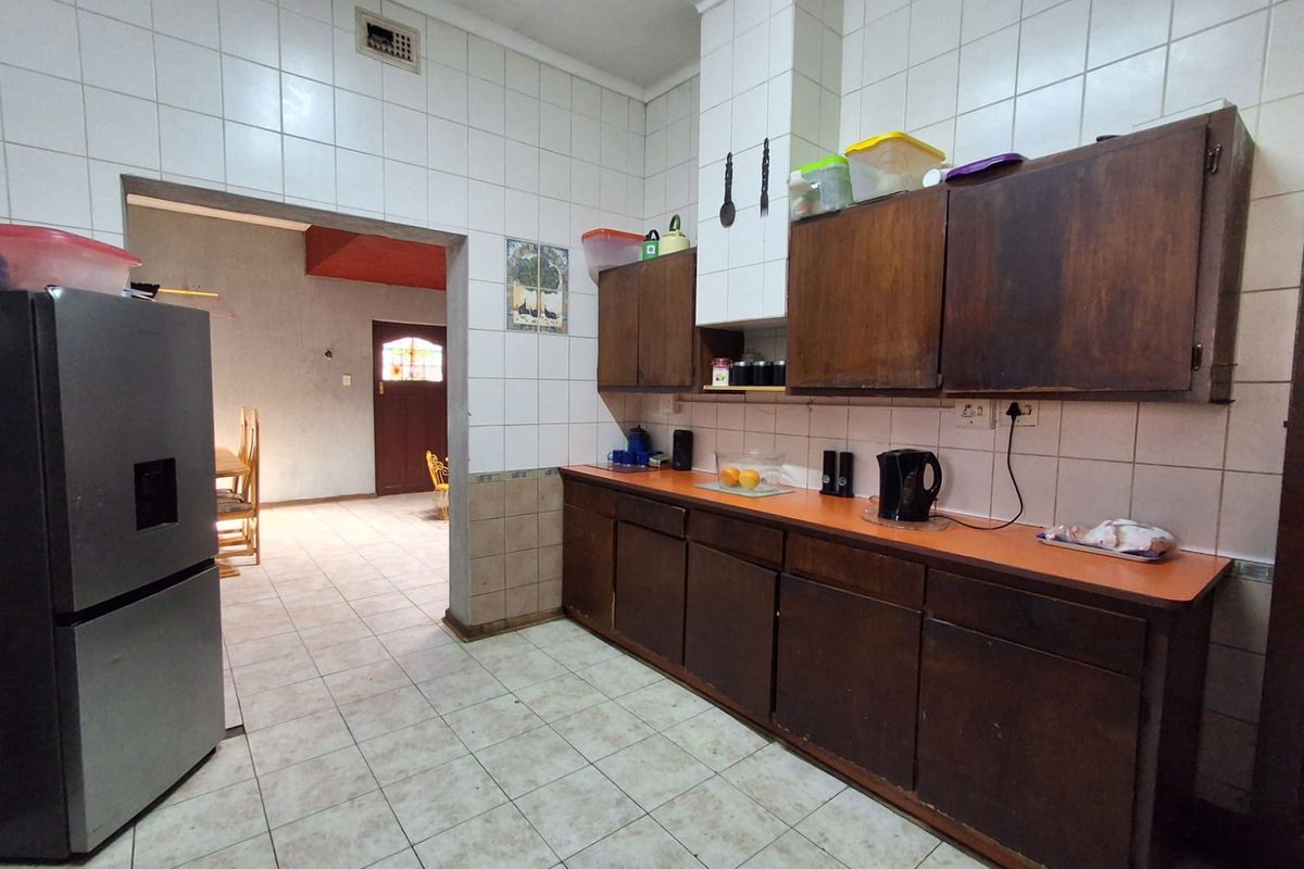 A dated kitchen featuring original wooden cabinetry, tiled walls, and tiled flooring, offering significant potential for a modern renovation and aesthetic update.