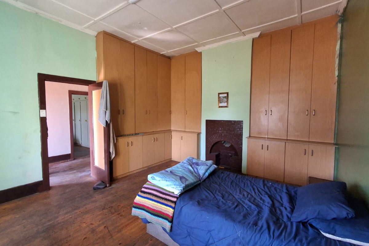 A bedroom featuring extensive built-in wooden cupboards, a brick fireplace, and original timber flooring, offering a dated aesthetic with potential for modernization.