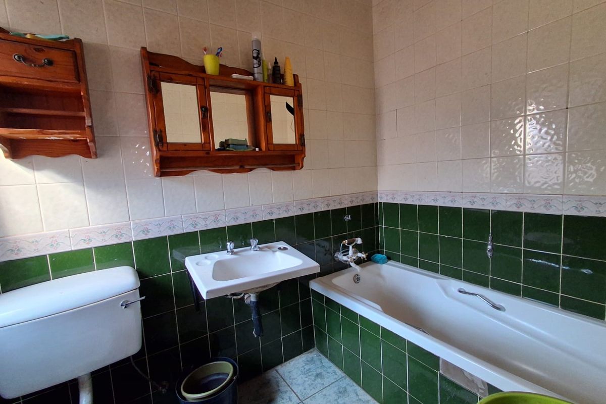 A dated bathroom featuring green and white wall tiling, a built-in bathtub, and a wall-mounted basin, requiring modernization of finishes and fixtures.