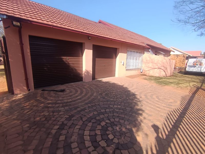 Front exterior view of the property featuring a double garage with roller shutter doors and a patterned paved driveway.