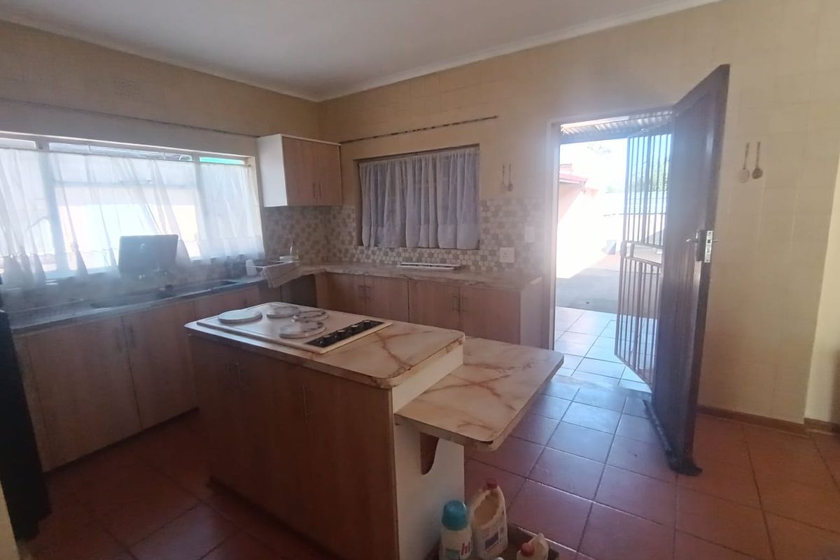 A functional kitchen featuring built-in cabinetry, a central island with a hob, tiled flooring, and direct access to the exterior via a security gate.