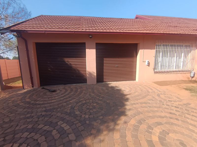 A double garage with brown roller doors and a paved driveway, featuring a tiled roof and security bars on the adjacent window.