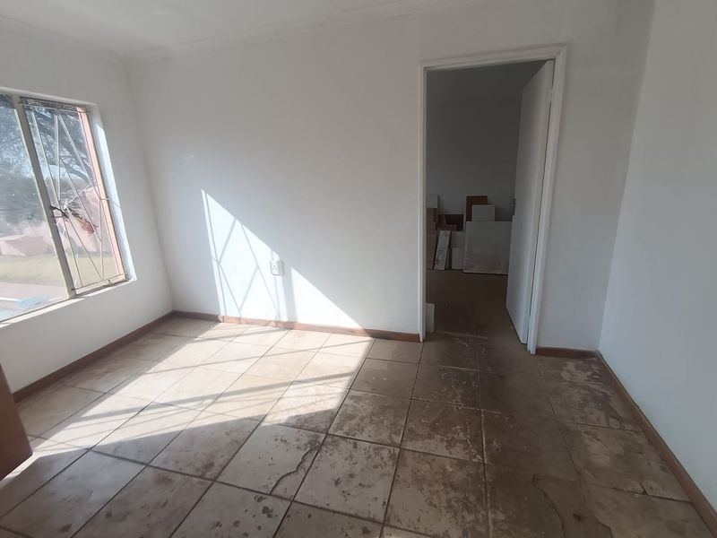An empty bedroom featuring tiled flooring, burglar bars on the window, and a doorway leading to an adjacent space.