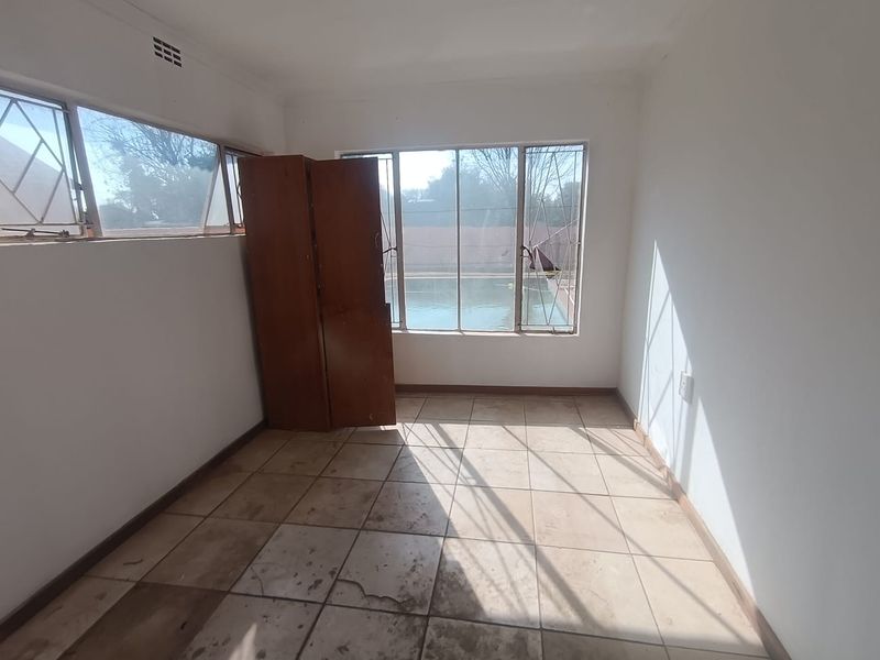 A vacant bedroom featuring tiled flooring, security bars on windows, and a view overlooking the swimming pool area.