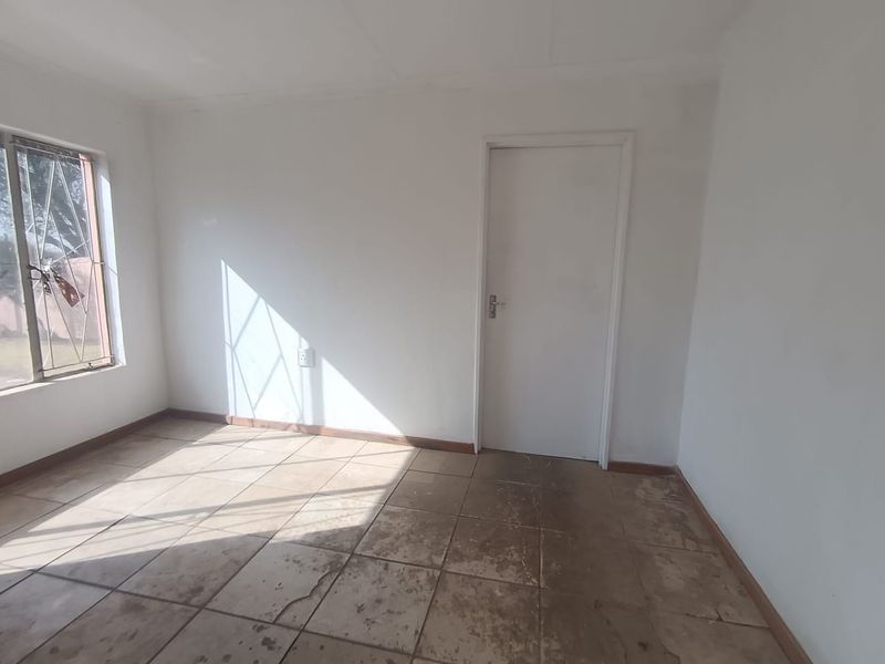 An empty bedroom featuring tiled flooring, a window with security bars, and a standard internal door, ready for renovation or staging.