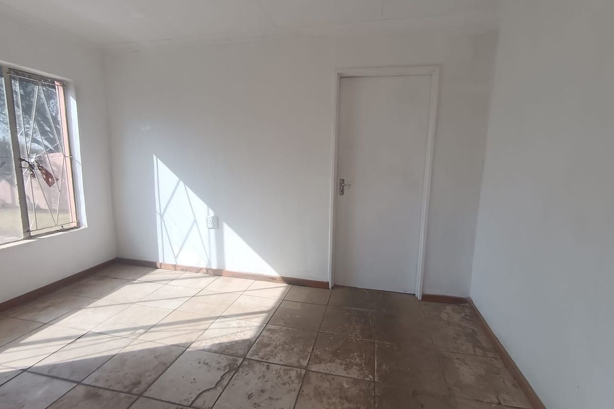 An empty bedroom featuring tiled flooring, a window with security bars, and a standard internal door, ready for renovation or staging.