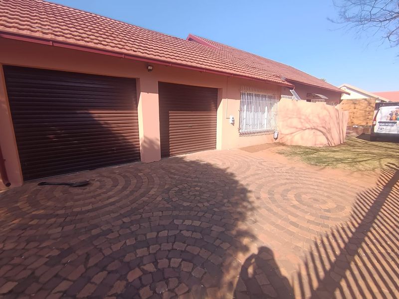 Front exterior view of the property featuring a double garage with roller shutter doors and a patterned paved driveway.