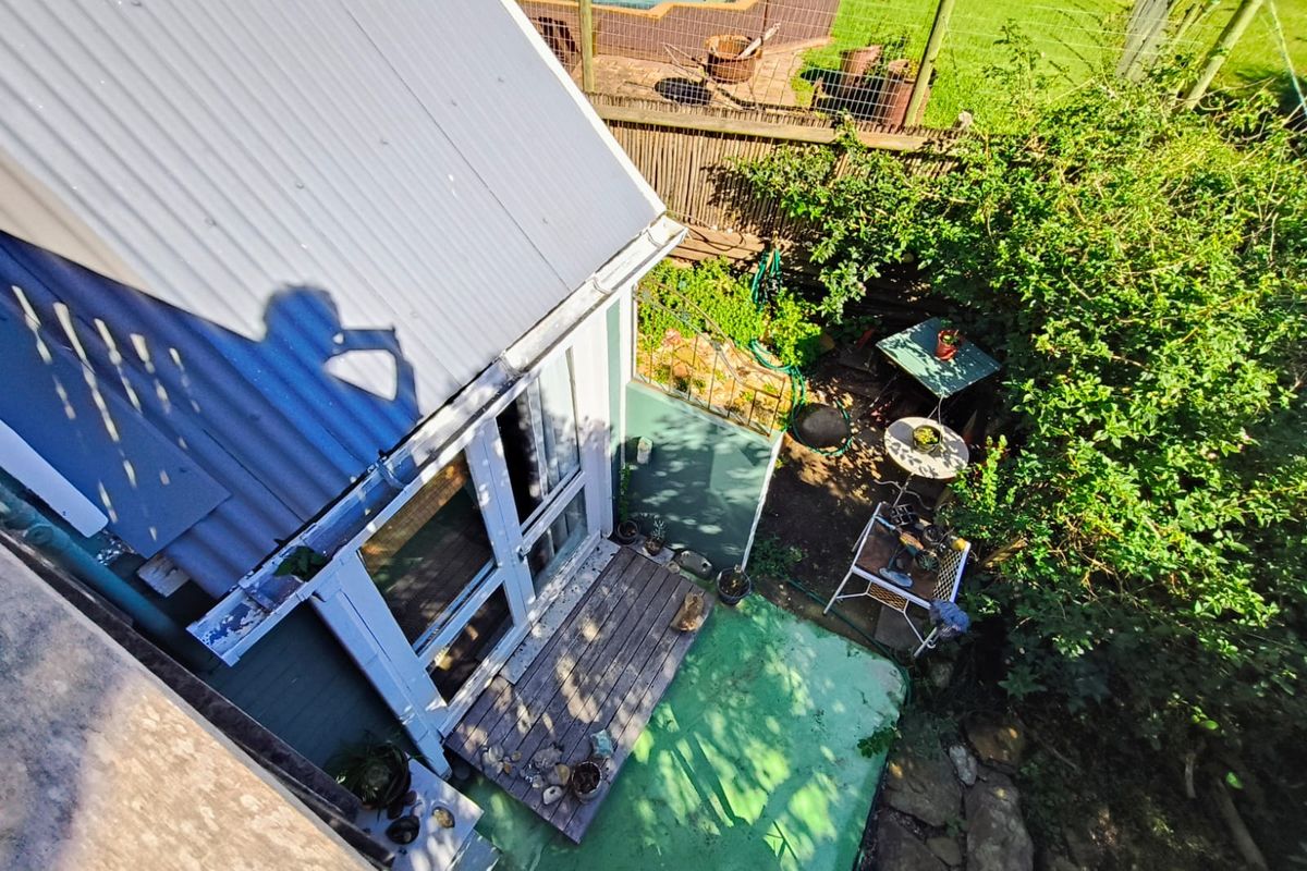 Aerial view of a property exterior featuring a corrugated metal roof, timber deck, and a swimming pool in the background.