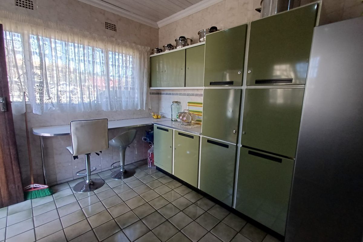 A dated kitchen featuring olive green built-in cabinetry, tiled flooring, and a breakfast bar area with tiled wall finishes.