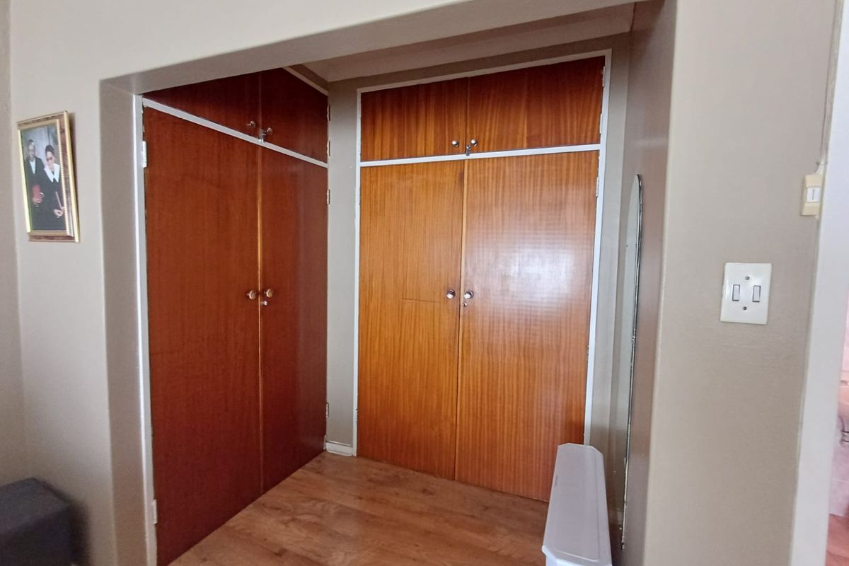 A bedroom area featuring classic wood-finish built-in cupboards with overhead storage and laminate flooring.