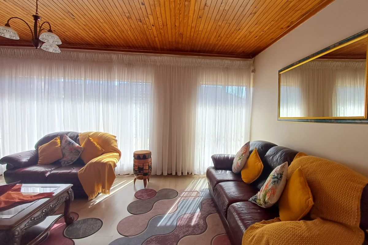 A bright living room featuring a warm timber tongue and groove ceiling, laminate flooring, and large windows that allow for ample natural light.