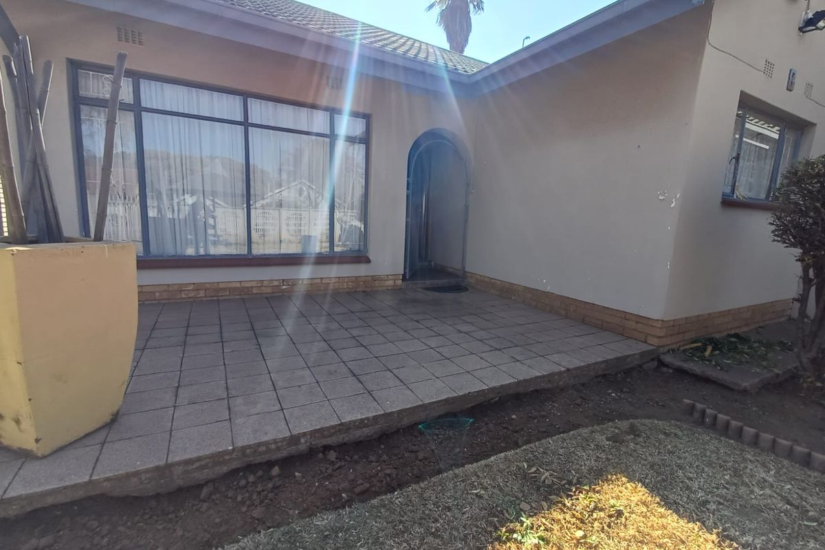 Rear exterior view featuring a tiled patio area, arched entrance, and large windows, showing potential for landscaping and minor exterior maintenance.