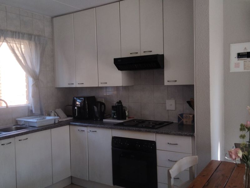 A functional kitchen featuring white cabinetry, a double sink, built-in oven with hob, extractor fan, and tiled backsplash.