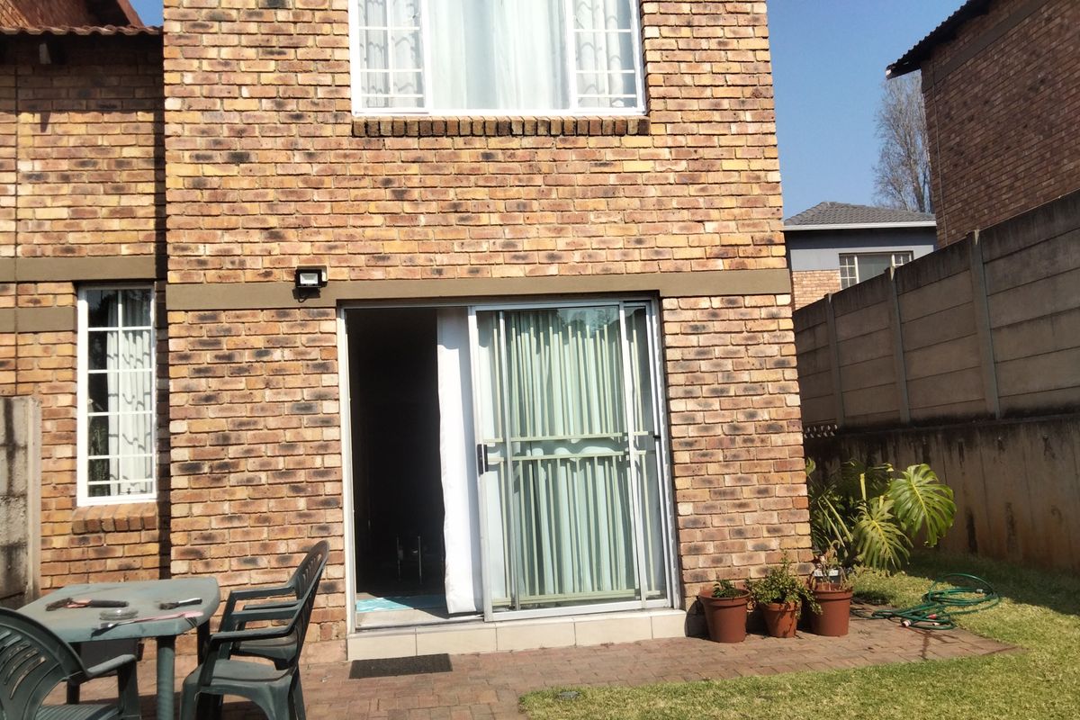Rear view of a face brick townhouse featuring a paved patio area and sliding glass door access to the interior.