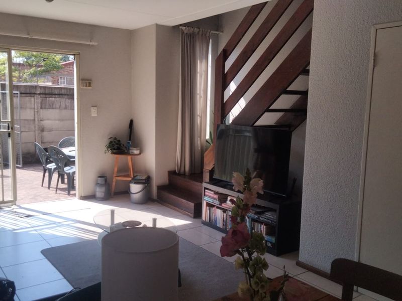 A living room featuring tiled flooring, a wooden staircase, and a sliding glass door providing access to an outdoor patio area.