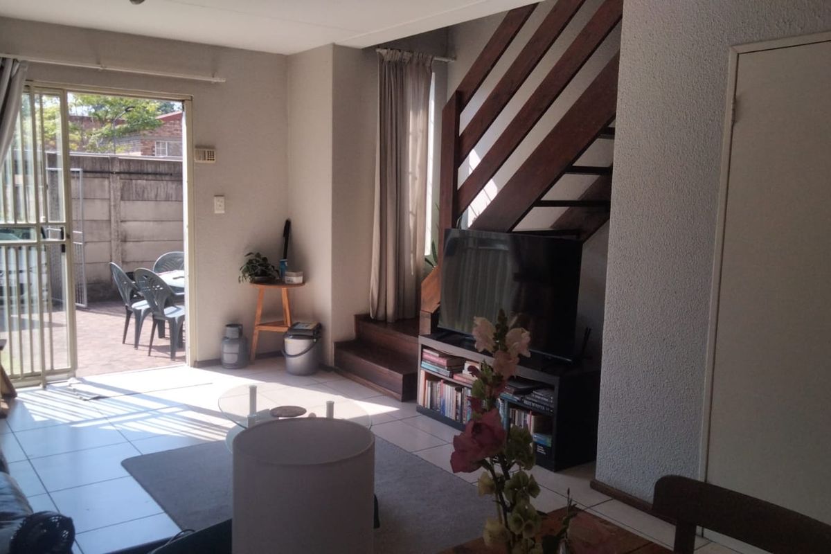 A living room featuring tiled flooring, a wooden staircase, and a sliding glass door providing access to an outdoor patio area.
