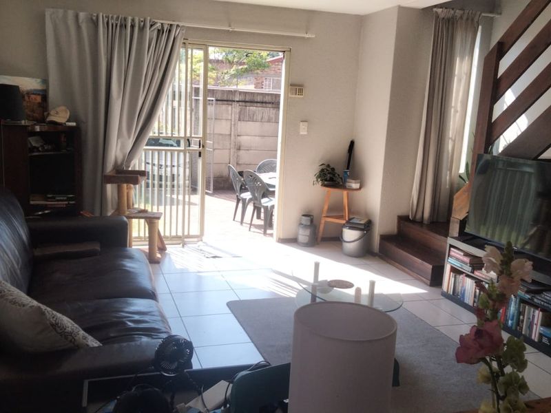 A living room featuring tiled flooring, a wooden staircase, and a sliding glass door providing access to an outdoor patio area.
