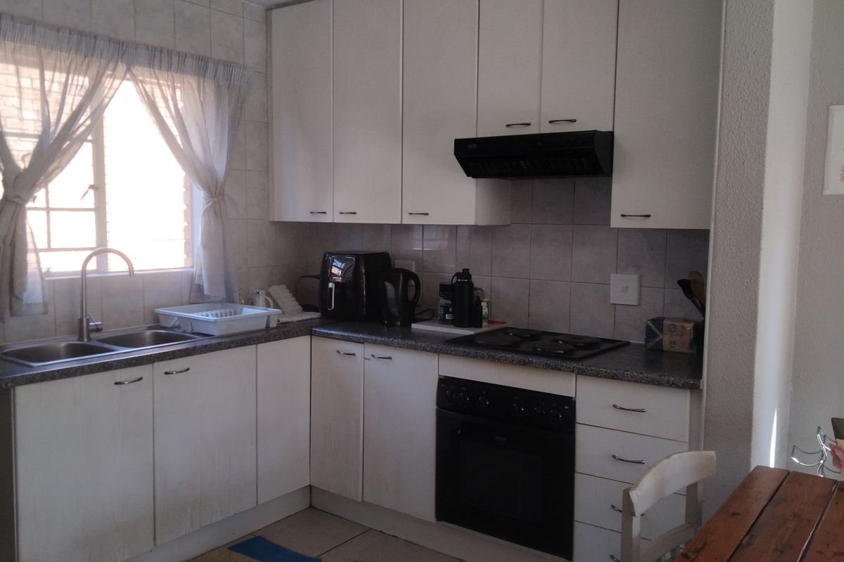 A functional kitchen featuring white cabinetry, a built-in oven with hob, extractor fan, and a double sink with tiled splashback.