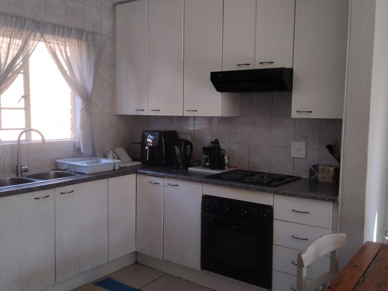 A functional kitchen featuring white cabinetry, a built-in oven with hob, extractor fan, and a double sink with tiled splashback.