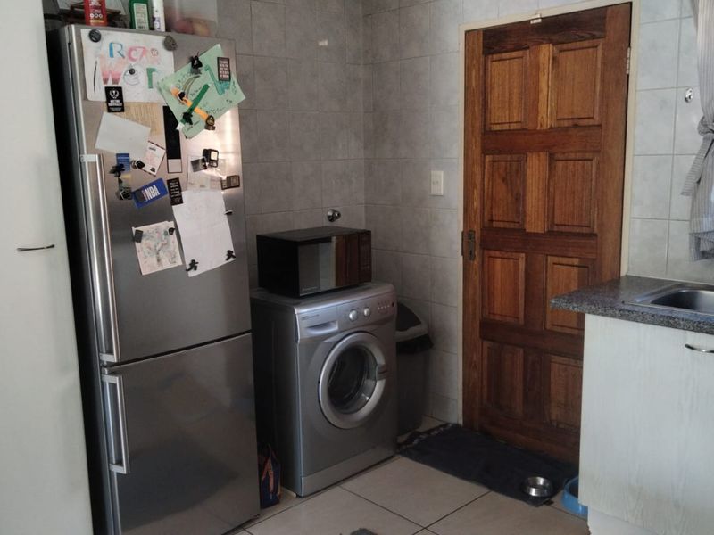 A functional kitchen area featuring tiled walls, tiled flooring, a stainless steel sink, and a solid wood door leading to an adjacent space.