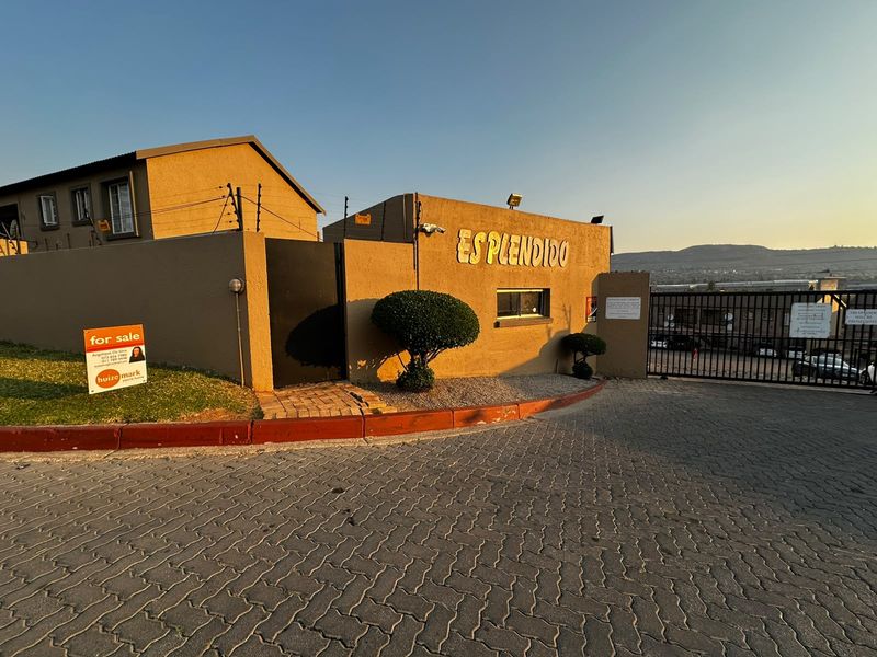 Front entrance view of the Esplendido complex featuring a paved driveway, secure perimeter wall with electric fencing, and gated access.