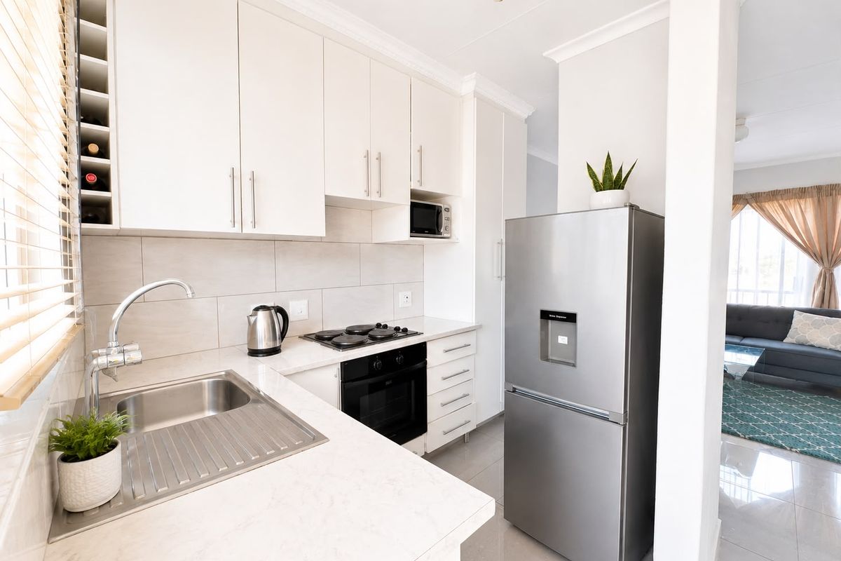 Modern kitchen featuring white cabinetry, stone countertops, integrated appliances, and a tiled backsplash, seamlessly flowing into the adjacent living area.