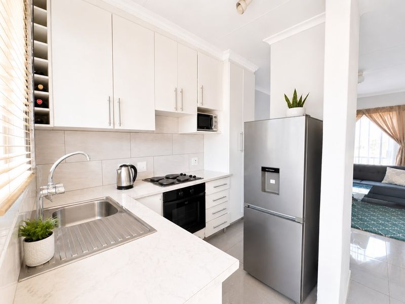 Modern kitchen featuring white cabinetry, stone countertops, integrated appliances, and a tiled backsplash, seamlessly flowing into the adjacent living area.