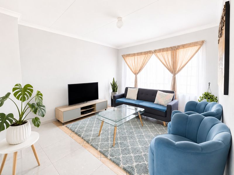 A bright and well-maintained living room featuring neutral tiled flooring, coved ceilings, and a large window allowing for ample natural light.